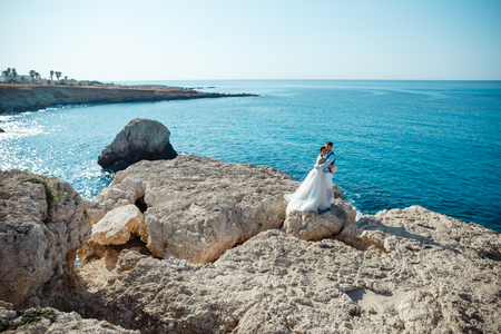 Beautiful smiling young bride and groom walking on the beach, kissing and having fun, wedding ceremony near the rocks and sea. Wedding ceremony on coast of Cyprusの写真素材