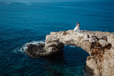 Beautiful smiling young bride and groom walking on the beach, kissing and having fun, wedding ceremony near the rocks and sea. Wedding ceremony on coast of Cyprusの写真素材