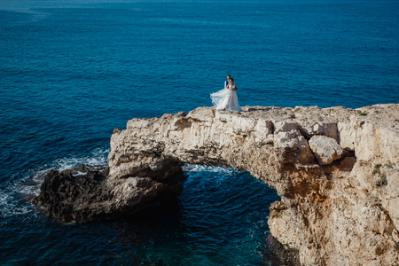 Beautiful smiling young bride and groom walking on the beach, kissing and having fun, wedding ceremony near the rocks and sea. Wedding ceremony on coast of Cyprusの写真素材