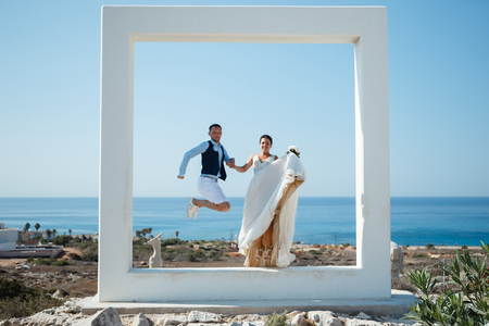Beautiful smiling young bride and groom walking on the beach, kissing and having fun, wedding ceremony near the rocks and sea. Wedding ceremony on coast of Cyprusの写真素材