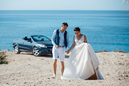 Beautiful smiling young bride and groom walking on the beach, kissing and having fun, wedding ceremony near the rocks and sea. Wedding ceremony on coast of Cyprusの写真素材