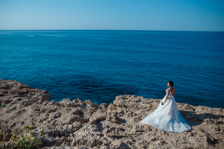 Beautiful smiling young bride and groom walking on the beach, kissing and having fun, wedding ceremony near the rocks and sea. Wedding ceremony on coast of Cyprusの写真素材