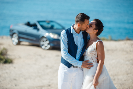 Beautiful smiling young bride and groom walking on the beach, kissing and having fun, wedding ceremony near the rocks and sea. Wedding ceremony on coast of Cyprusの写真素材