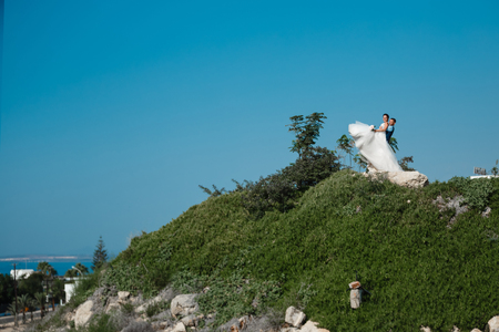 Beautiful smiling young bride and groom walking on the beach, kissing and having fun, wedding ceremony near the rocks and sea. Wedding ceremony on coast of Cyprusの写真素材