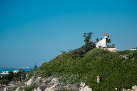Beautiful smiling young bride and groom walking on the beach, kissing and having fun, wedding ceremony near the rocks and sea. Wedding ceremony on coast of Cyprusの写真素材