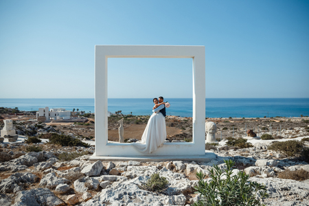 Beautiful smiling young bride and groom walking on the beach, kissing and having fun, wedding ceremony near the rocks and sea. Wedding ceremony on coast of Cyprusの写真素材