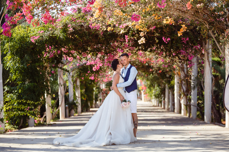 Beautiful smiling young bride and groom walking on the beach, kissing and having fun, wedding ceremony near the rocks and sea. Wedding ceremony on coast of Cyprusの写真素材