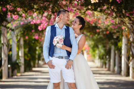 Beautiful smiling young bride and groom walking on the beach, kissing and having fun, wedding ceremony near the rocks and sea. Wedding ceremony on coast of Cyprusの写真素材