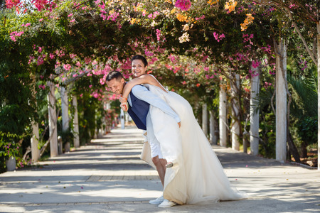 Beautiful smiling young bride and groom walking on the beach, kissing and having fun, wedding ceremony near the rocks and sea. Wedding ceremony on coast of Cyprusの写真素材