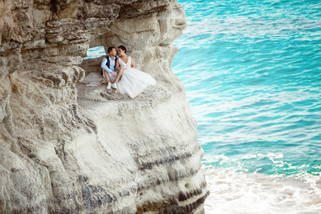 Beautiful smiling young bride and groom walking on the beach, kissing and having fun, wedding ceremony near the rocks and sea. Wedding ceremony on coast of Cyprusの写真素材