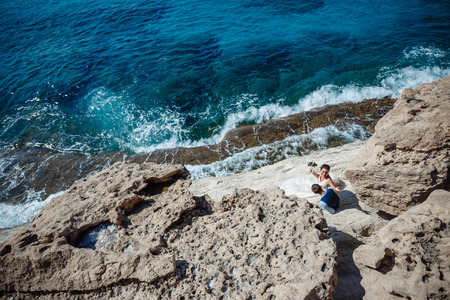 Beautiful smiling young bride and groom walking on the beach, kissing and having fun, wedding ceremony near the rocks and sea. Wedding ceremony on coast of Cyprusの写真素材