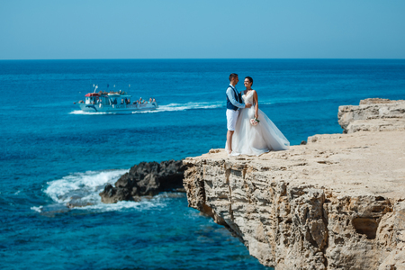 Beautiful smiling young bride and groom walking on the beach, kissing and having fun, wedding ceremony near the rocks and sea. Wedding ceremony on coast of Cyprusの写真素材