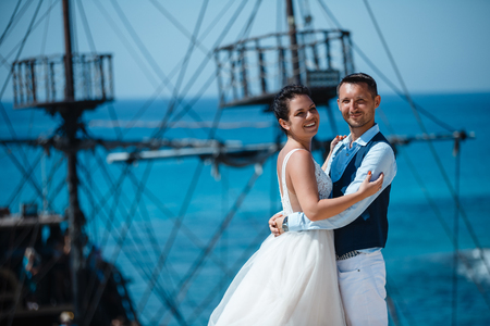 Beautiful smiling young bride and groom walking on the beach, kissing and having fun, wedding ceremony near the rocks and sea. Wedding ceremony on coast of Cyprusの写真素材