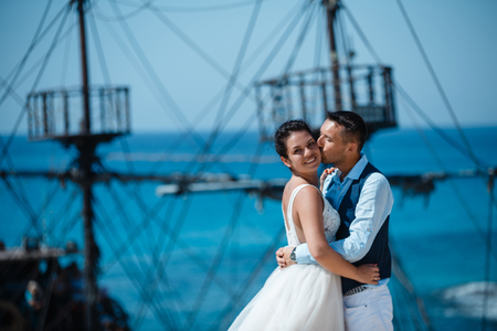 Beautiful smiling young bride and groom walking on the beach, kissing and having fun, wedding ceremony near the rocks and sea. Wedding ceremony on coast of Cyprusの写真素材