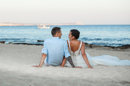 Beautiful smiling young bride and groom walking on the beach, kissing and having fun, wedding ceremony near the rocks and sea. Wedding ceremony on coast of Cyprusの写真素材