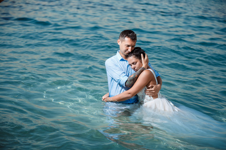 Beautiful smiling young bride and groom walking on the beach, kissing and having fun, wedding ceremony near the rocks and sea. Wedding ceremony on coast of Cyprusの写真素材
