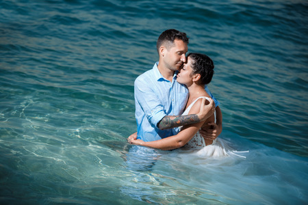 Beautiful smiling young bride and groom walking on the beach, kissing and having fun, wedding ceremony near the rocks and sea. Wedding ceremony on coast of Cyprusの写真素材