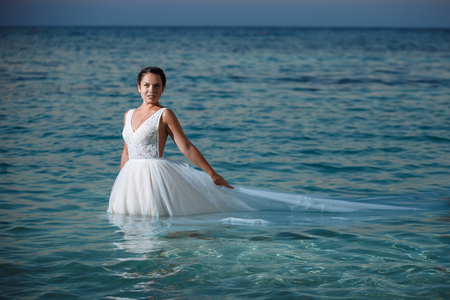 Beautiful smiling young bride and groom walking on the beach, kissing and having fun, wedding ceremony near the rocks and sea. Wedding ceremony on coast of Cyprusの写真素材