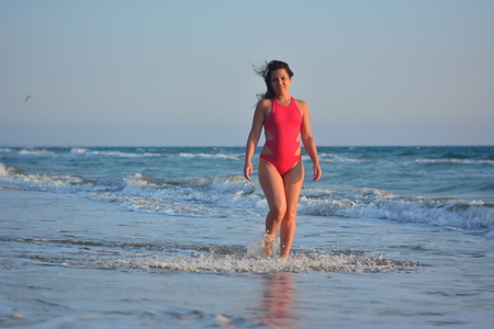 Beautiful happy brunette girl posing on the beach in a red bathing suit.の写真素材