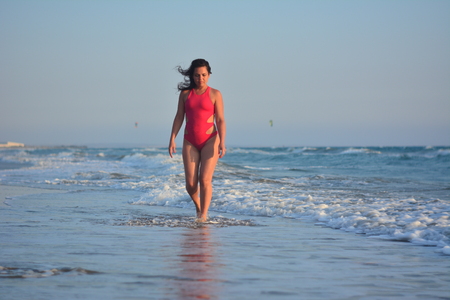Beautiful happy brunette girl posing on the beach in a red bathing suit.の写真素材