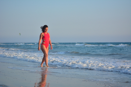 Beautiful happy brunette girl posing on the beach in a red bathing suit.の写真素材