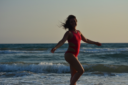 Beautiful happy brunette girl posing on the beach in a red bathing suit.の写真素材