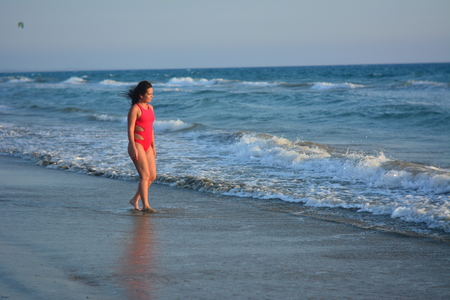 Beautiful happy brunette girl posing on the beach in a red bathing suit.の写真素材
