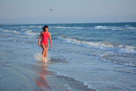 Beautiful happy brunette girl posing on the beach in a red bathing suit.の写真素材