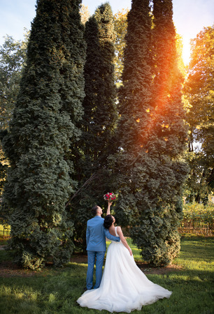 Wedding couple on the nature is hugging each other. Beautiful model girl in white dress. Man in suit. Beauty bride with groom. Female and male portrait. Woman with lace veil. Lady and guy outdoorsの写真素材