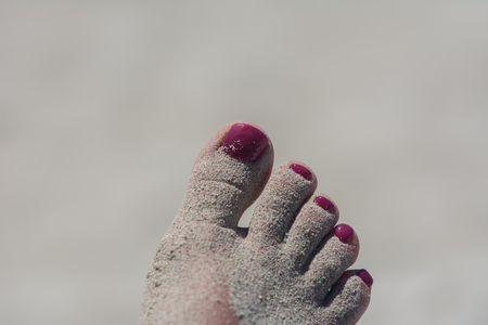 Woman feet with red toenails on natural beach sandの写真素材