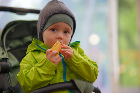 A two-year-old boy in a baby carriage with a slice of cheeseの写真素材