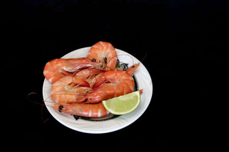 Boiled king prawns with lime on the plate in isolated over blackの写真素材