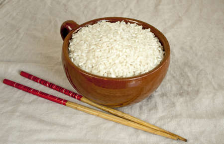 Dry oval rice in  ceramic mug and chopsticksの写真素材
