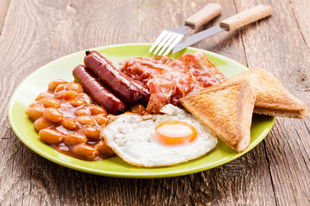 English breakfast with bacon, sausage, fried egg, baked beans and tea or orange juiceの写真素材