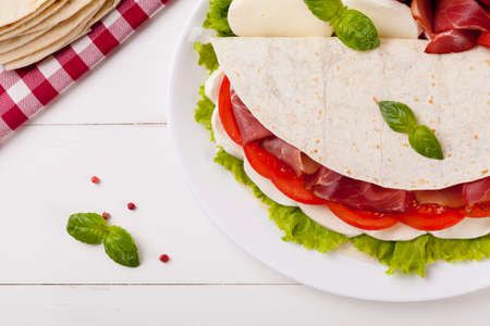 Italian Piadina Romagnola with mozzarella, ham and vegetables on white woodboardの写真素材