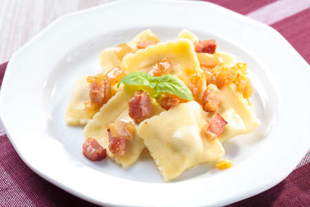 Portion of ravioli with onion and bacon on white plateの写真素材