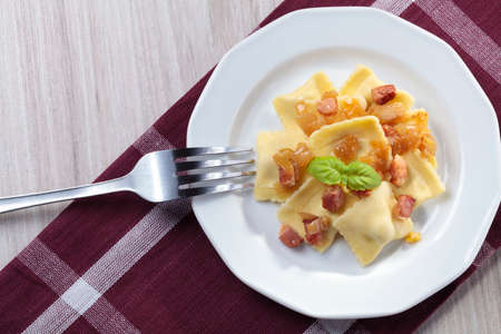 Portion of ravioli with onion and bacon on white plateの写真素材