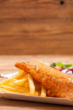 Fried fish and chips on a paper tray - Natural wooden backgroundの写真素材