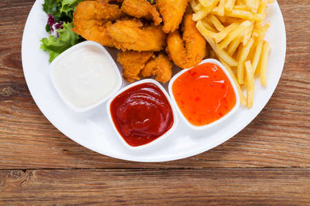 Nuggets and chips on a plate served with dip and salads on a wooden boardの写真素材