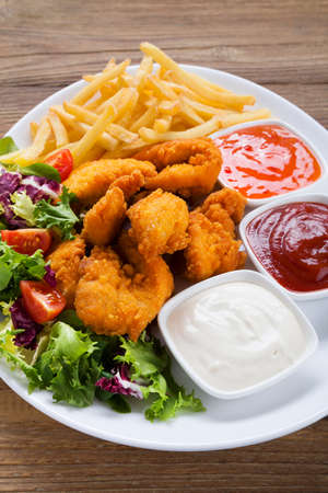 Nuggets and chips on a plate served with dip and salads on a wooden boardの写真素材