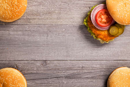 Home made chicken burger with lettuce, tomato and onion on wooden boardの写真素材