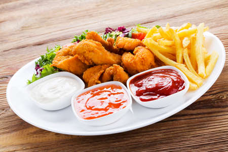 Nuggets and chips on a plate served with dip and salads on a wooden boardの写真素材