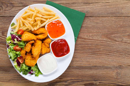 Nuggets and chips on a plate served with dip and salads on a wooden boardの写真素材