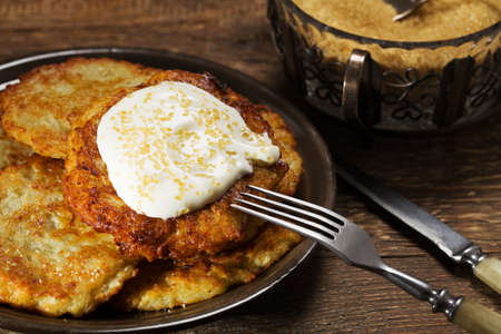 Homemade potato pancakes served with sour cream and brown sugar from cane on wooden board.