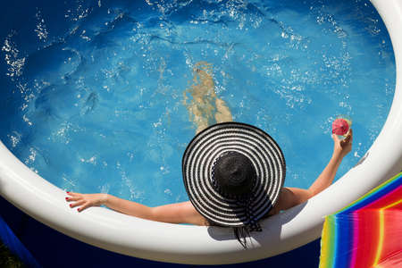 Young woman in a straw hat relaxing in the garden pool.
