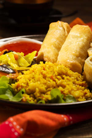 Portion baked spring rolls with vegetables and rice on a plate, served with sauce.の写真素材