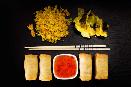 Baked spring rolls with deep, rice and vegetables, on a black plateの写真素材