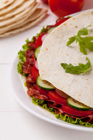 Italian Piadina Romagnola with salami and vegetables on white woodboardの写真素材