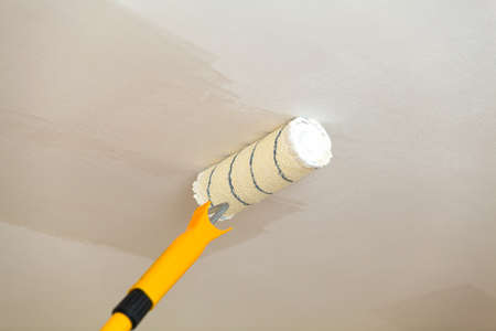 Painting the ceiling a roller with white paint.の写真素材