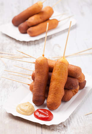 Corn dog. Sausage baked in corn dough served with ketchup and mustard on a paper tray.